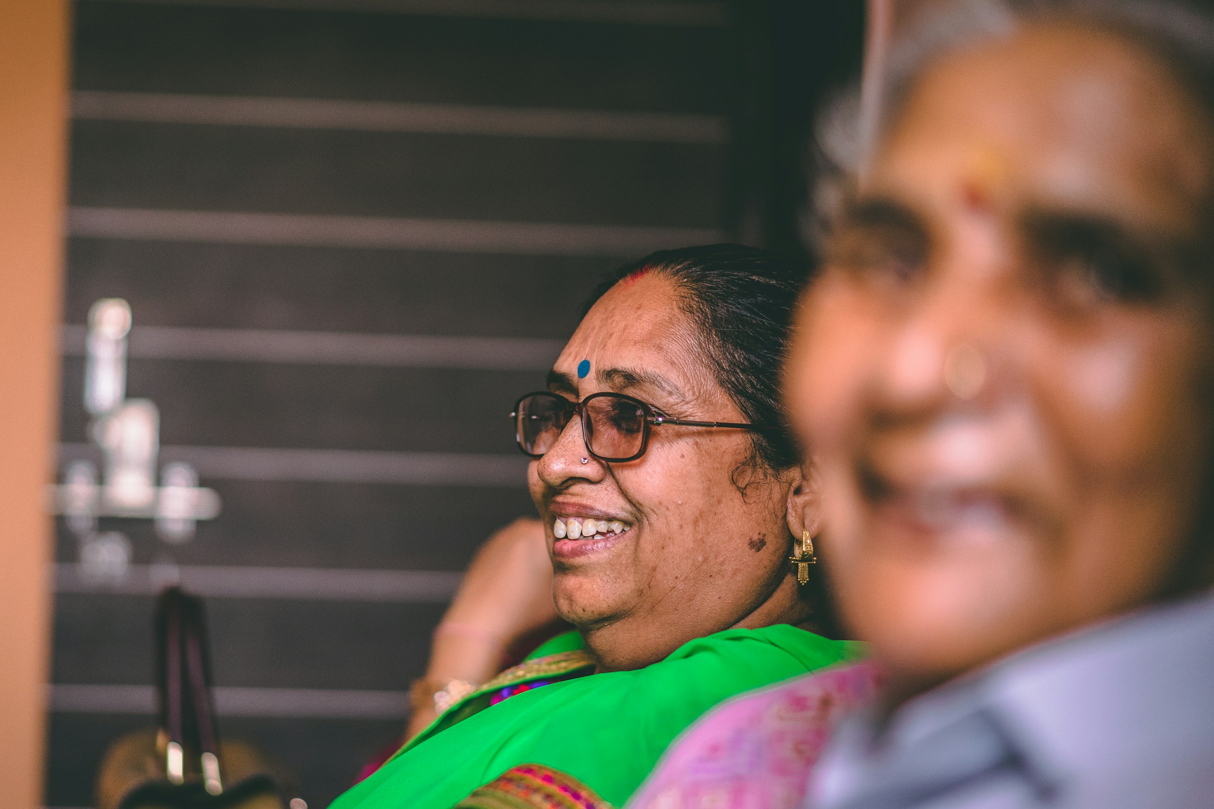 Two women in their sixties talking together, one in a green sari and glasses.